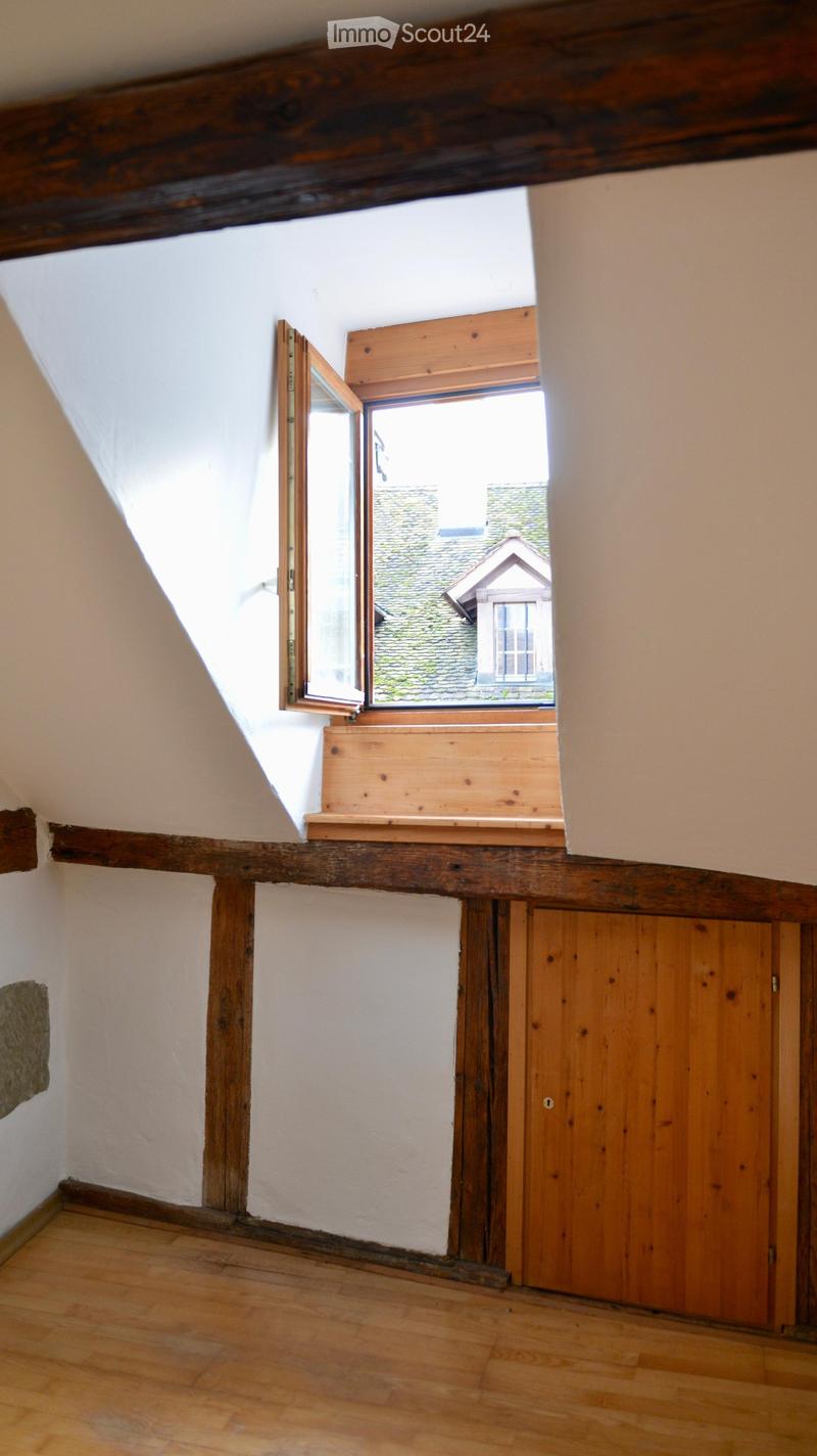 empty attic room with slanted wooden ceiling, white walls, wooden door, small attic window