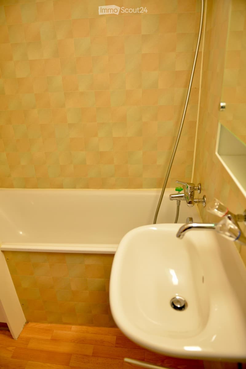 a bathtub, sink, tiles, water supply pipes, a mirror, a wooden floor