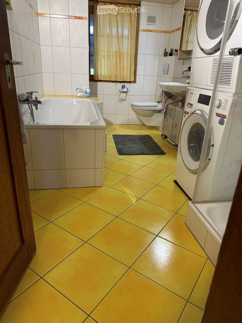 Bathroom with yellow tiled floor, white tiled walls, bathtub, toilet, sink, washing machine, and a small rug.