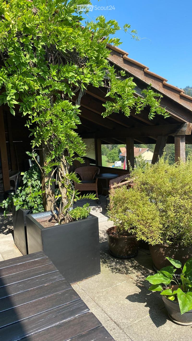 A covered outdoor patio with wooden decking, potted plants, and a small seating area with a table and chairs.