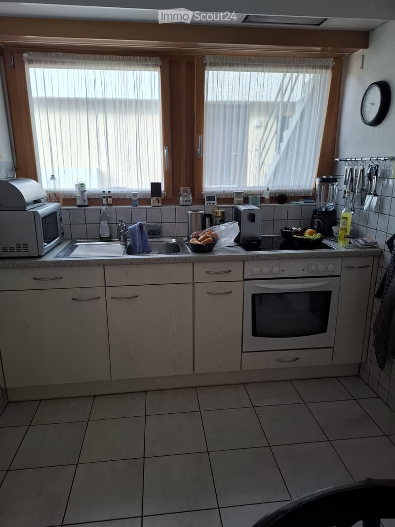 The kitchen features light wooden cabinets, a white tiled backsplash, and a granite countertop. Appliances include a microwave, oven, and coffee maker. A sink with a faucet is visible, along with various kitchen items such as a blender, toaster, and cups