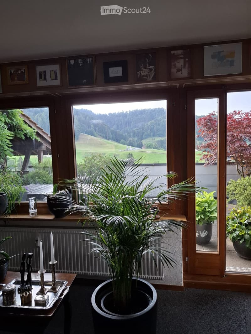 Bright living room with large windows offering a scenic view, decorated with plants, candles, and artwork.