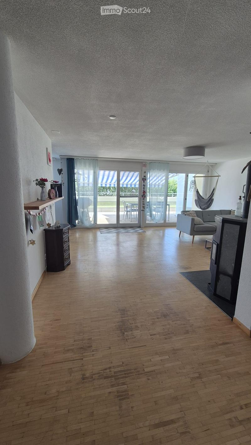 Bright living room with wooden flooring, large sliding glass doors leading to a balcony, a grey sofa, a small table, and a fireplace.