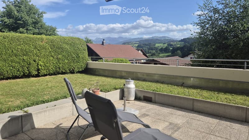Balcony with a view of mountains, featuring two chairs, a small table, and a milk can as a decorative element.