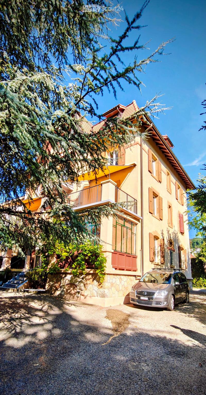 Two-story yellow house with red shutters, stone lower level, and a parked car in front.