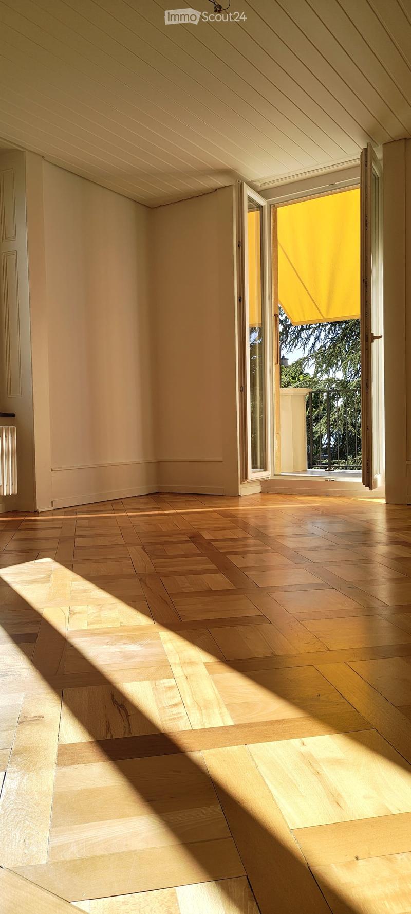 Empty room with wooden flooring and large windows allowing natural light to enter, creating shadows on the floor.