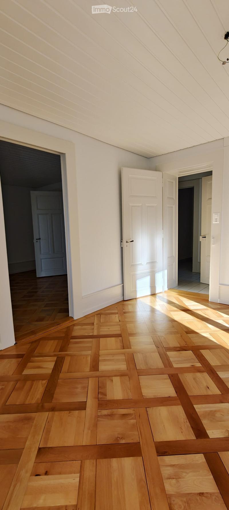 Empty room with wooden flooring and white walls, featuring multiple doors leading to other spaces.