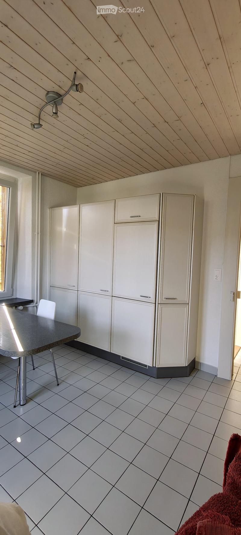 Modern kitchen with white cabinets, tiled floor, and a small dining area featuring a table and chair.