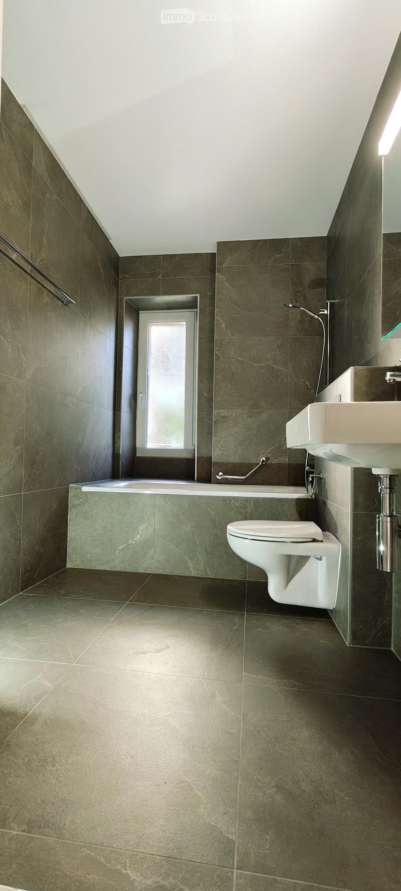 Modern bathroom with dark green marble tiles, a bathtub, toilet, and sink, featuring a frosted window and built-in storage.