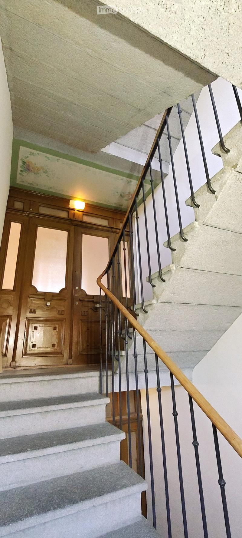 Staircase with wooden handrail, metal balustrade, and grey carpeted steps leading to a wooden door at the end.