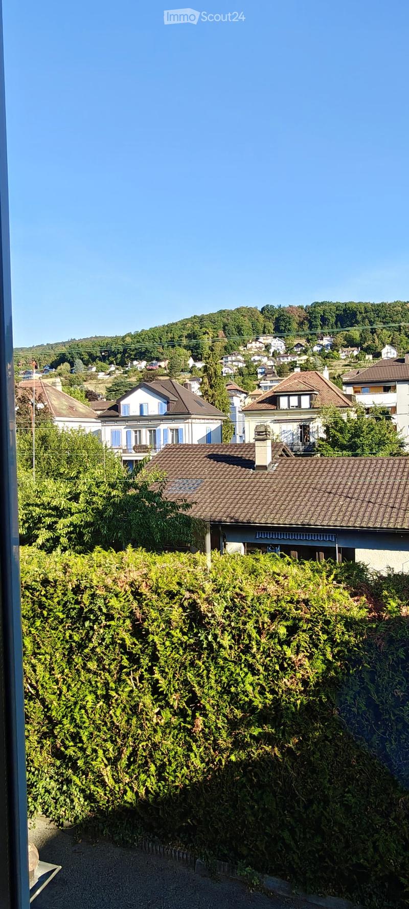 View of a residential area with houses, lush greenery, and a clear blue sky.