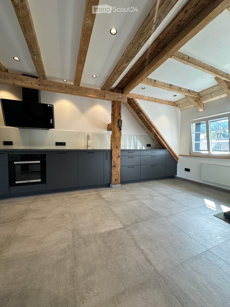 Modern kitchen with exposed wooden beams, grey cabinets, tiled floor, and large windows.