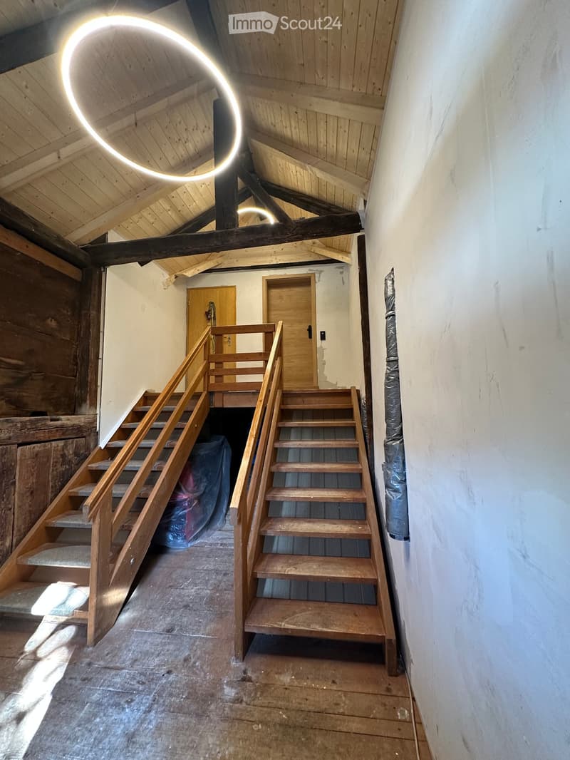 Empty wooden staircase leading to a loft area with exposed wooden beams and a circular light fixture on the ceiling.