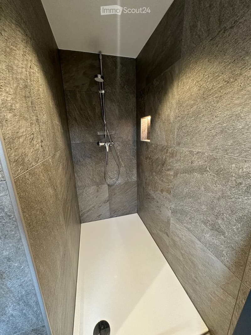 Modern shower area with grey marble tiles, a built-in showerhead, and a small window for natural light.