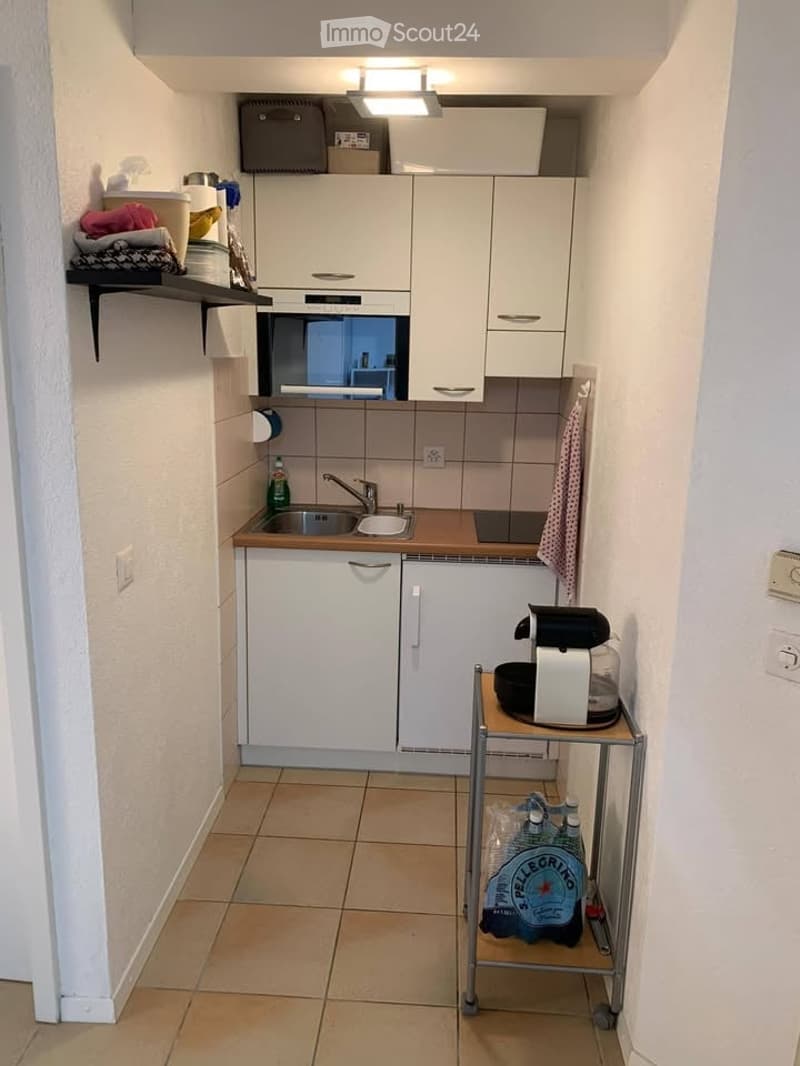 Compact kitchen with white cabinets, a sink, microwave, dishwasher, and a small cart holding a coffee maker and water bottles.