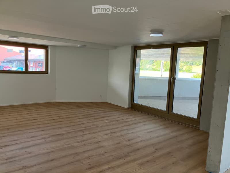 Empty room with wooden flooring, large windows, and sliding glass doors leading to a balcony.