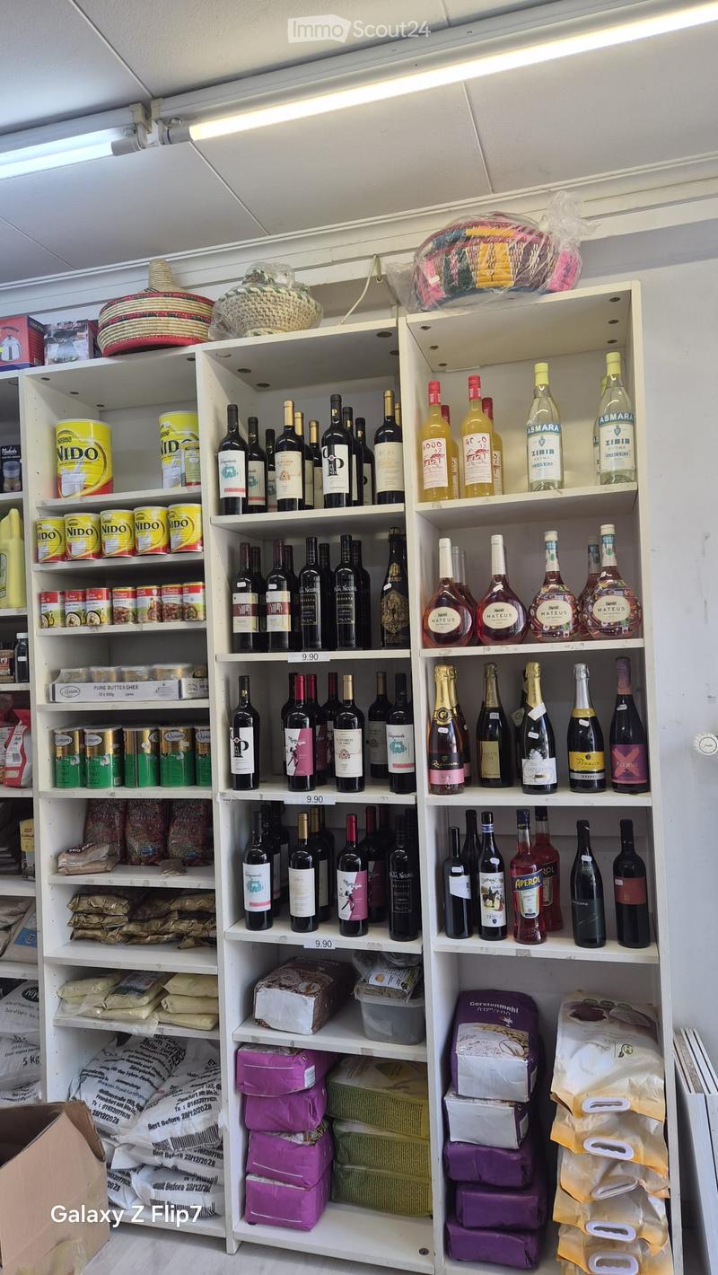 A well-organized store shelf displaying various products including wine bottles, canned goods, cheese, bread, and packaged items. The shelves are neatly arranged with price tags visible.
