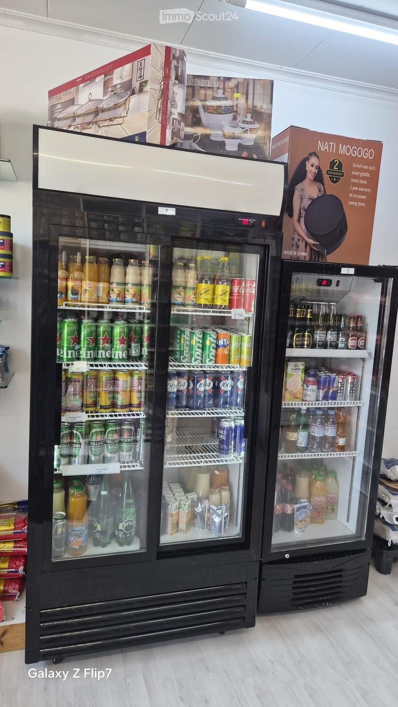 Three black commercial refrigerators stocked with various beverages including soda, beer, and juice. Boxes of tea sets and kitchen appliances are visible in the background.