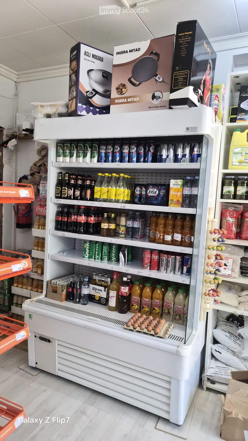 A store display featuring a refrigerator stocked with various beverages and a tray of eggs on the bottom shelf. Surrounding shelves hold additional products.