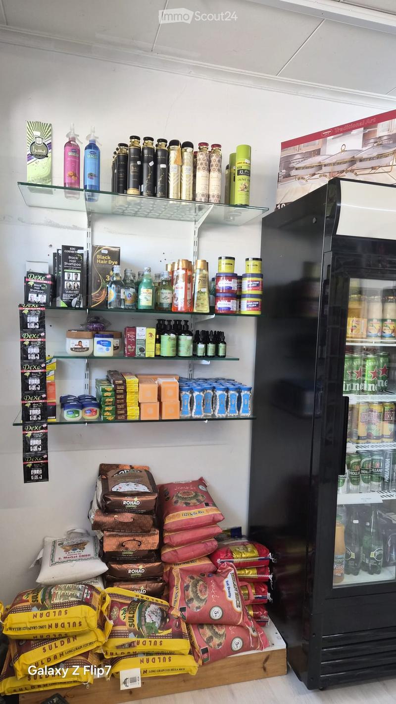 A small convenience store with shelves stocked with various products, including hair care items, canned goods, and packaged food items. A refrigerator is visible on the right side.
