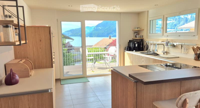 Modern kitchen with large windows and balcony, tiled floor, counter, sink, stove, large table and chairs, mountains view
