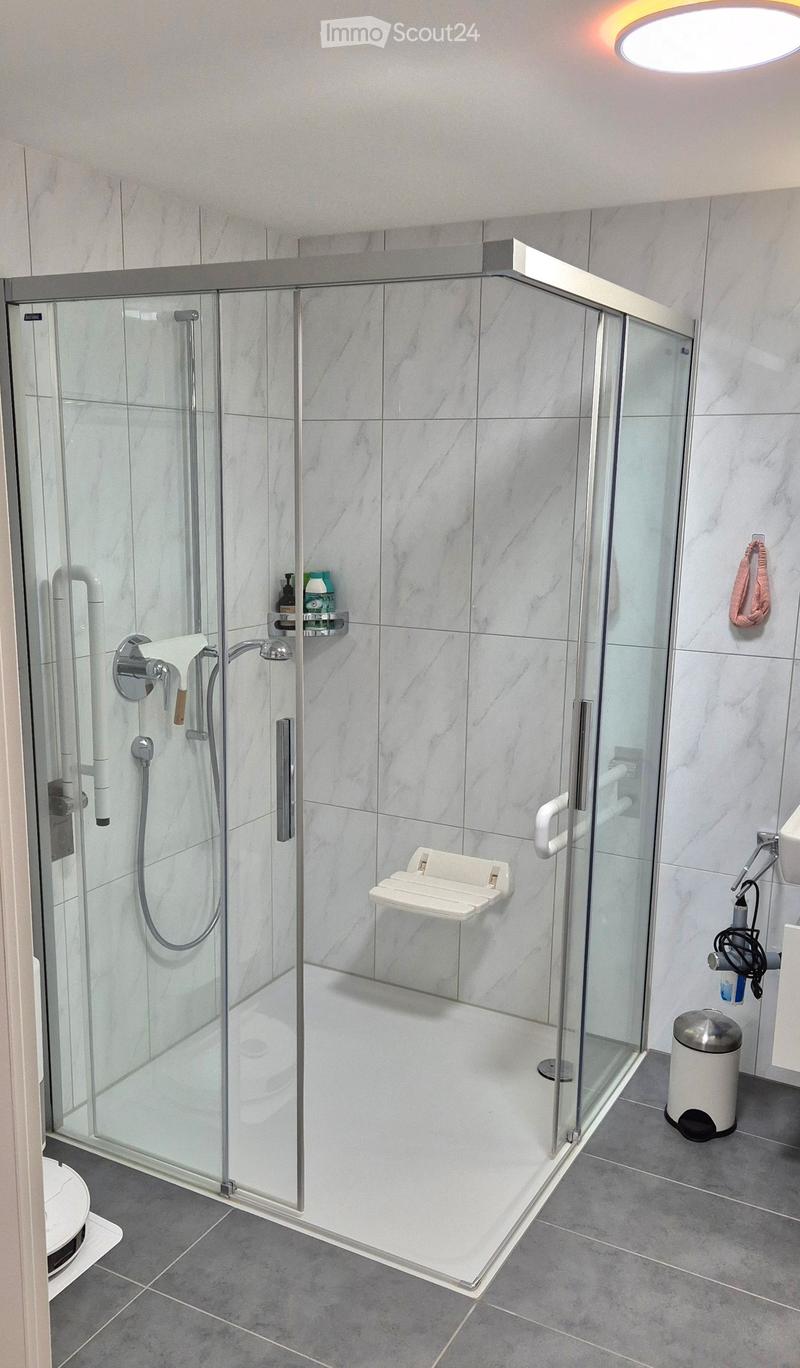 Glass walk-in shower with seating, handheld shower, tiled floor, white cabinetry, round ceiling light