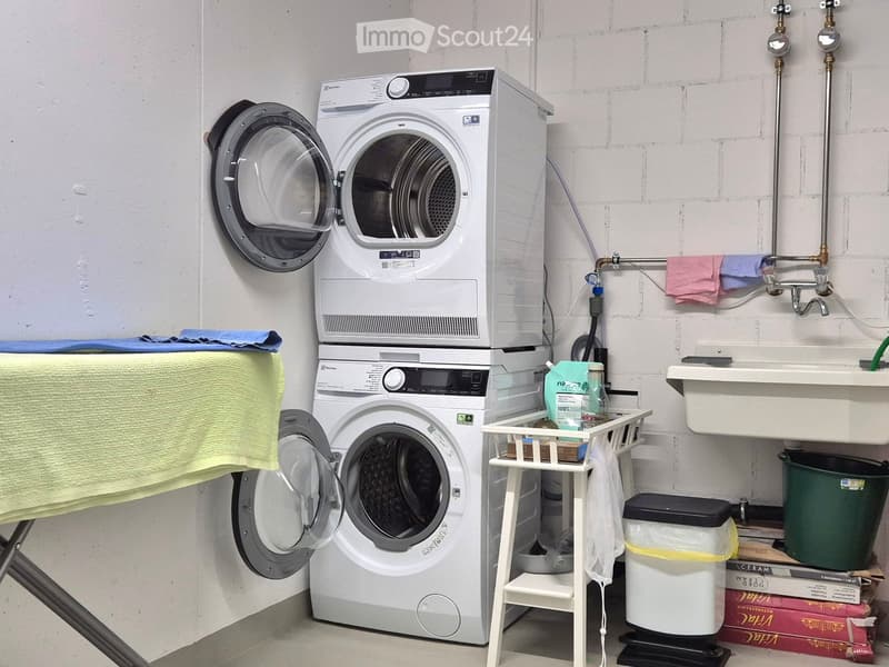 Laundry area, 2 washing machines, ironing table, sink, green trash bin, boxes