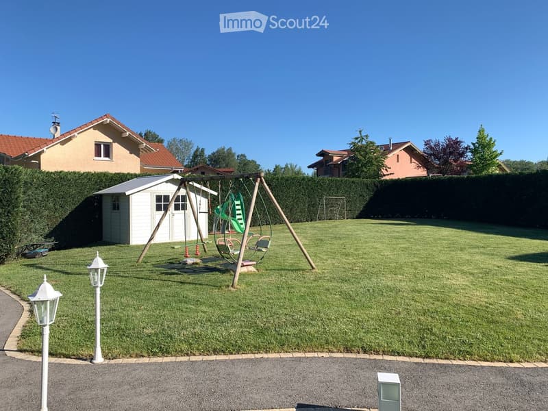 Well-maintained lawn with a swing set, slide, and play equipment, surrounded by hedges and neighboring houses.