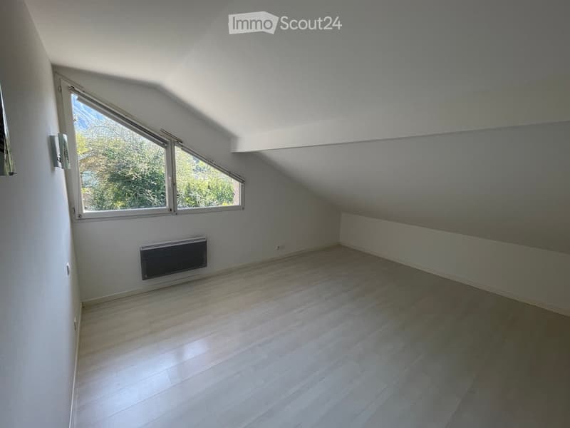 Empty attic room with wooden flooring, white walls, large windows, and a built-in radiator.