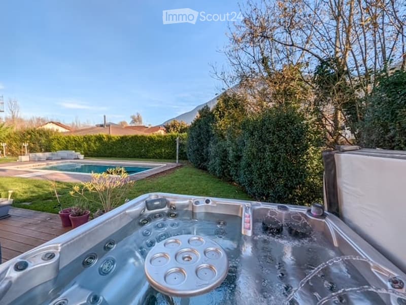 Private backyard with a hot tub, swimming pool, neatly trimmed hedges, and a wooden deck.