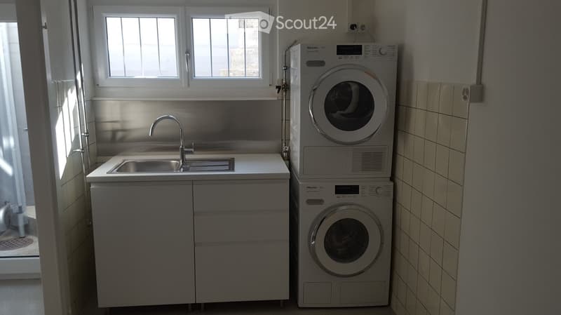 Compact bathroom with a sink, faucet, and stacked washing machine and dryer unit. The space features tiled walls and a window for natural light.