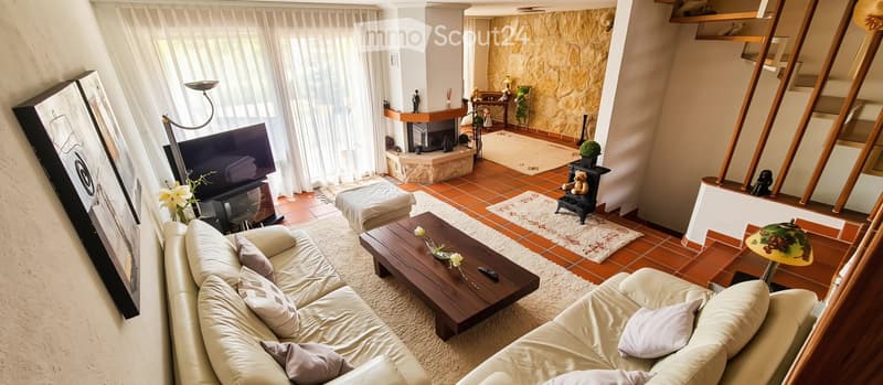 Spacious living room with a beige sectional sofa, wooden coffee table, ottoman, fireplace, and large windows with white curtains.