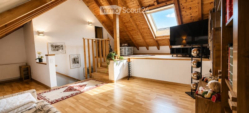 Bright, wooden-floored attic room with exposed wooden beams, skylight, sofa, TV, small table, and decorative items.