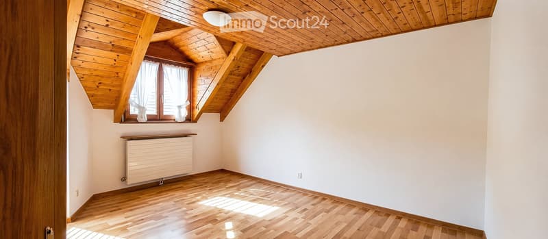 Empty room with wooden floor, white walls, wooden ceiling beams, and a window with white curtains. No furniture or equipment present.