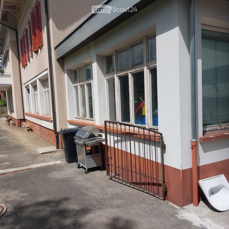 Outdoor area next to a building with a grill, trash bin, and a small gate.
