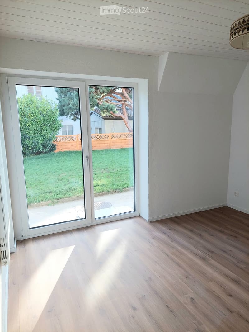 Empty room with wooden flooring and large sliding glass doors leading to a garden area.
