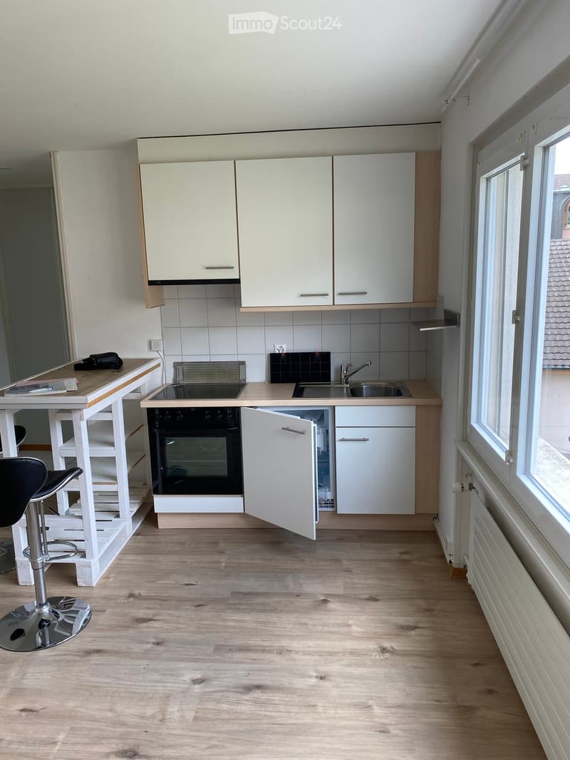 Modern kitchen with white cabinets, wooden countertops, stainless steel sink, and built-in oven. Includes a small table with a stool.