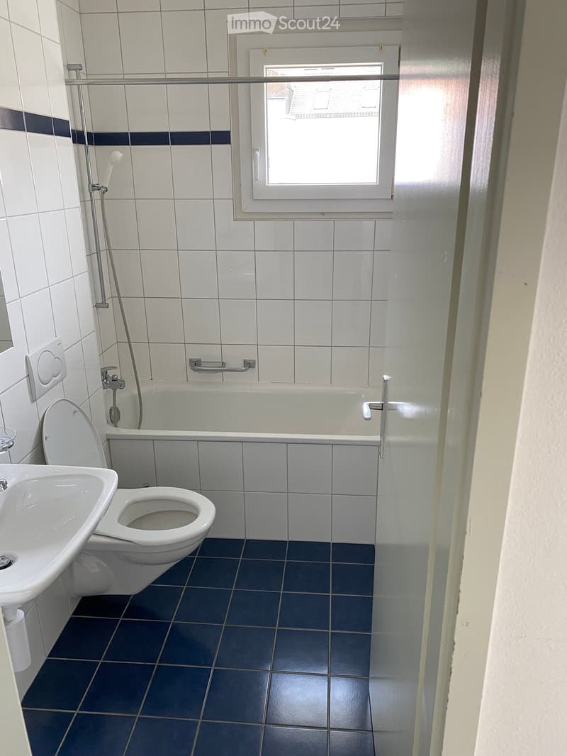 Bathroom with white tiled walls, blue tiled floor, toilet, sink, bathtub, and shower hose.