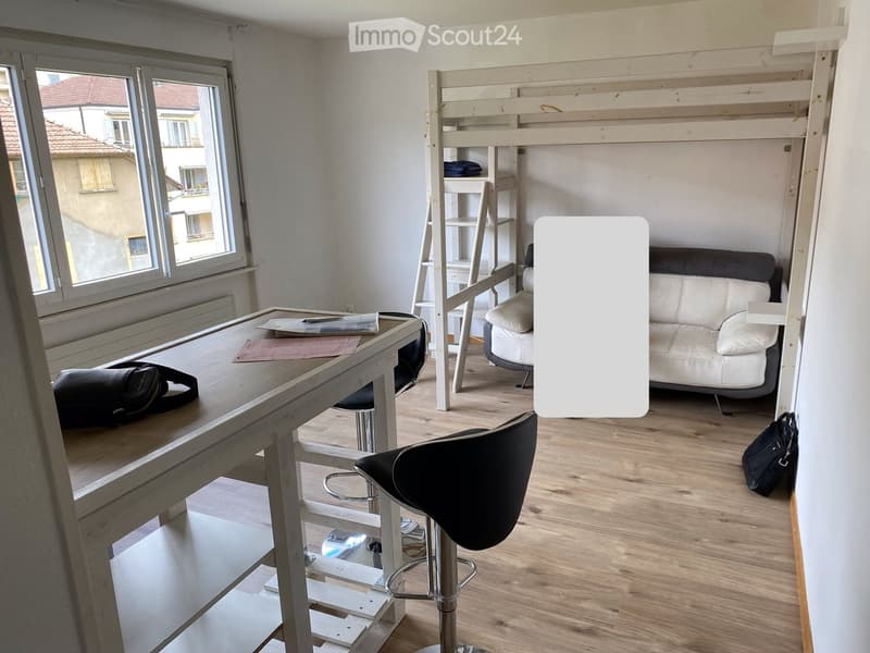 A furnished room with a sofa, a desk, a stool chair, a stool, a backpack, and a bed.