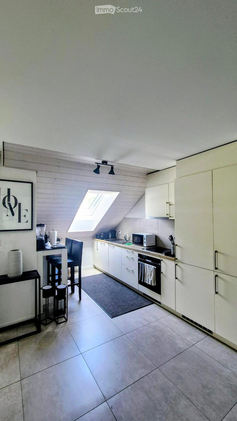 Modern kitchen with white cabinets, stainless steel appliances, a small dining area with stools, and a skylight window above the sink.