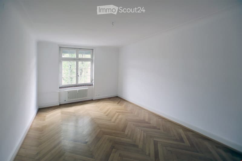 Empty room, white walls, parquet floors, large window with white shutters, white radiator under window.