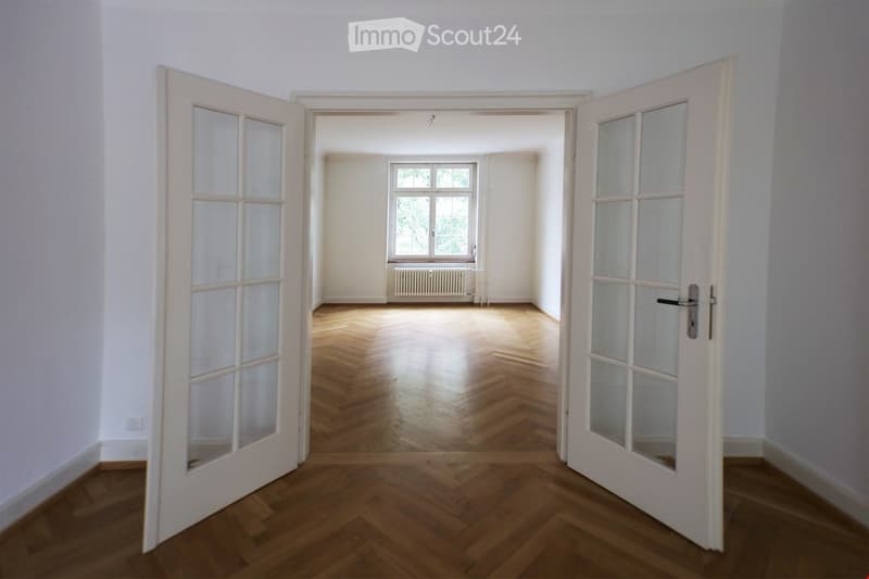 wood floor, white walls, radiator, two open doors, windows with a view
