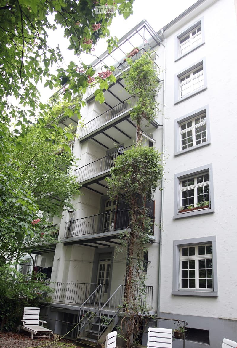 white building with balconies, two chairs outside, potted plants, stairs, vines growing on wall