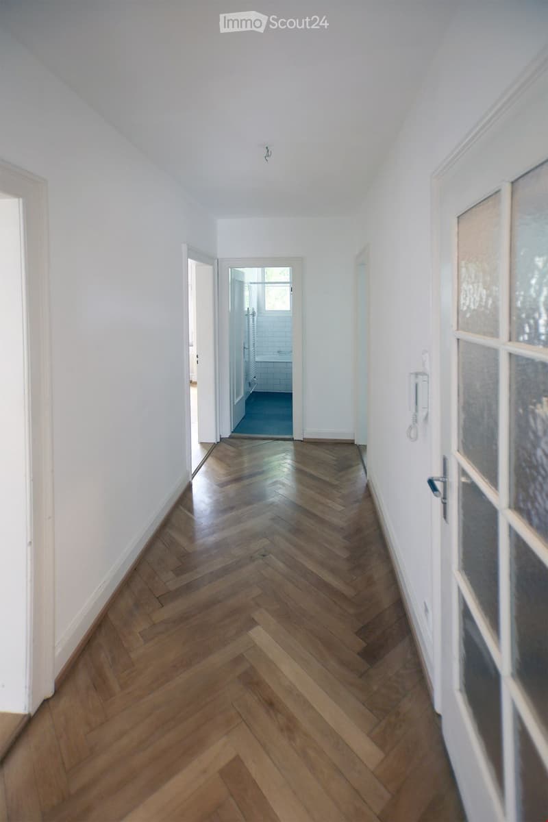 Hardwood floors, white walls, doors leading to different rooms, entrance to bathroom visible, phone mounted on wall.