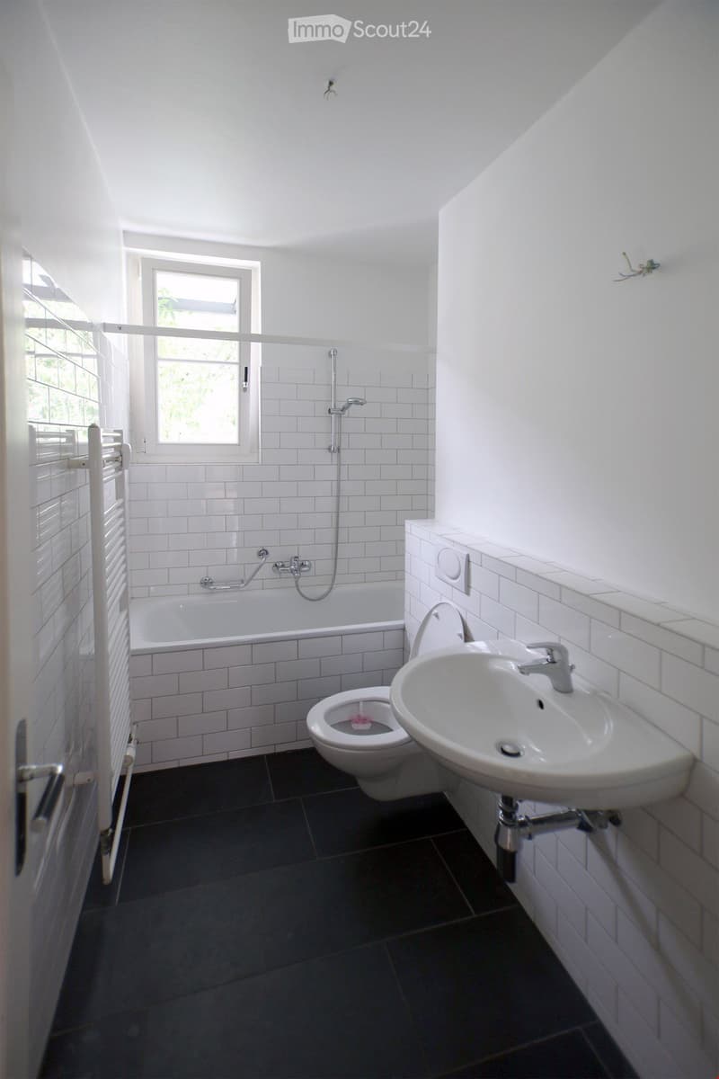 Modern white tile bathroom with bathtub, toilet, sink, shower head, towel rack, white tile floor and walls