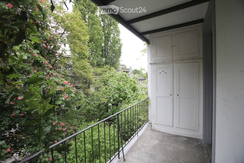 balcony with black railings, white wooden cabinet with doors, concrete floor, greenery outside