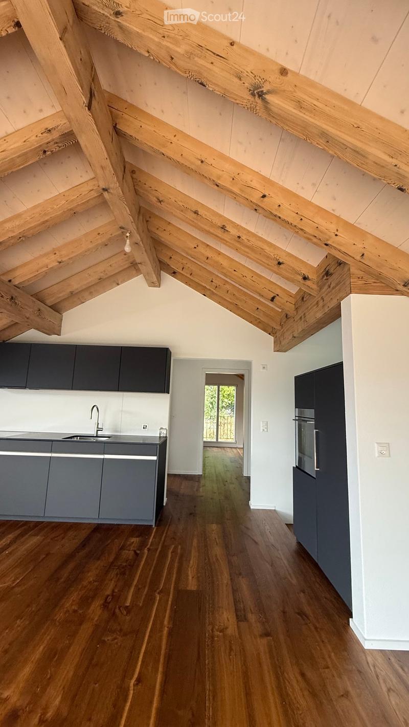 Open-plan kitchen and living area with exposed wooden beams, grey cabinets, wooden flooring, and a sink with a faucet.