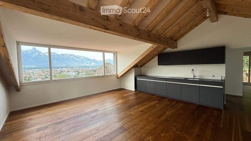 Modern kitchen with wooden flooring, dark grey cabinets, and a large window offering a scenic mountain view.