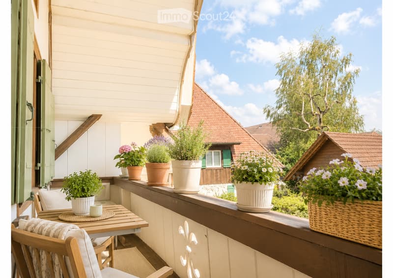 Balcony with wooden furniture, potted plants, and a view of a residential area with houses and trees.