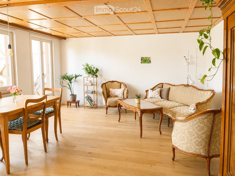 Bright living room with wooden flooring, a large sofa, armchairs, a dining table with chairs, a bookshelf, and potted plants.